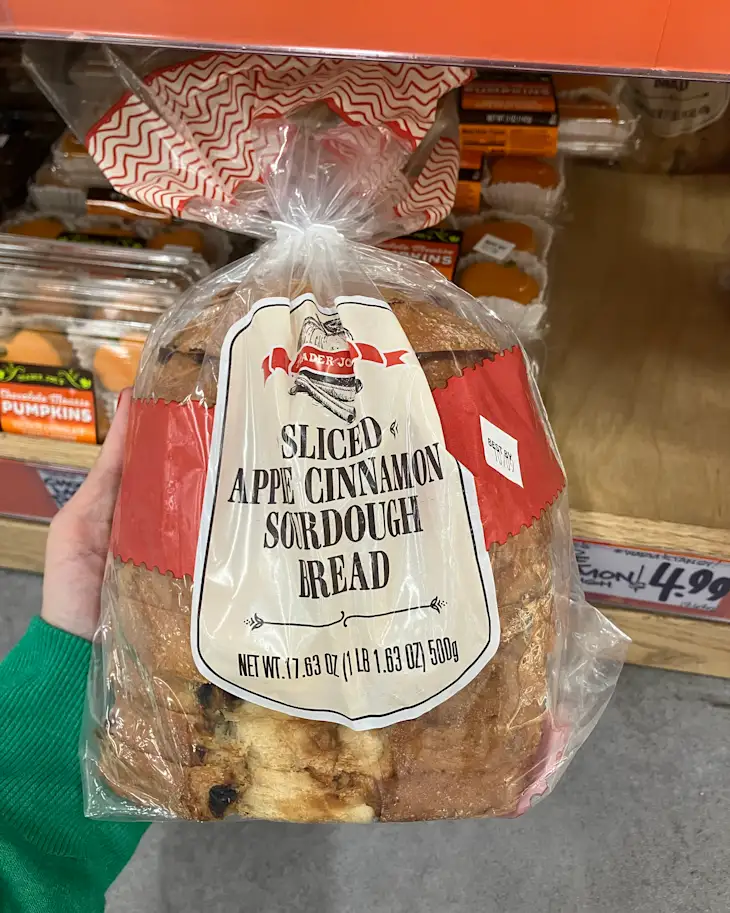 Sliced apple cinnamon sourdough bread in a clear bag, held in a hand, with other products in the background.